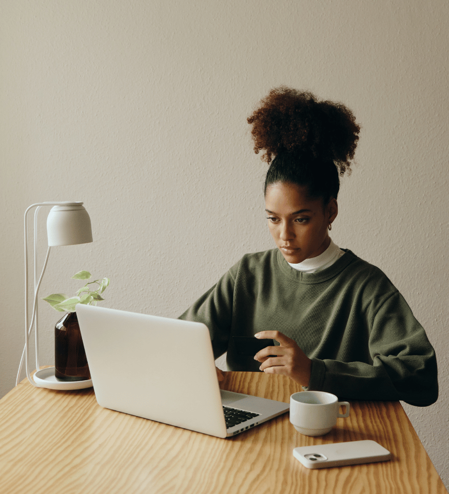 Young woman working on her laptop at home with her coffee beside her